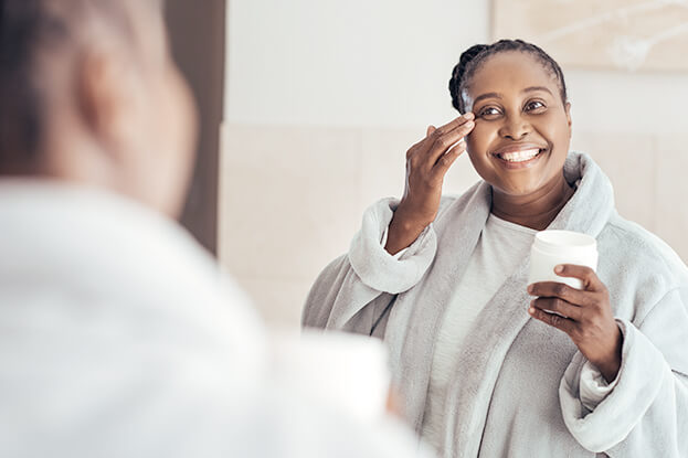 Smiling happy woman applying moisturizer in bathroom