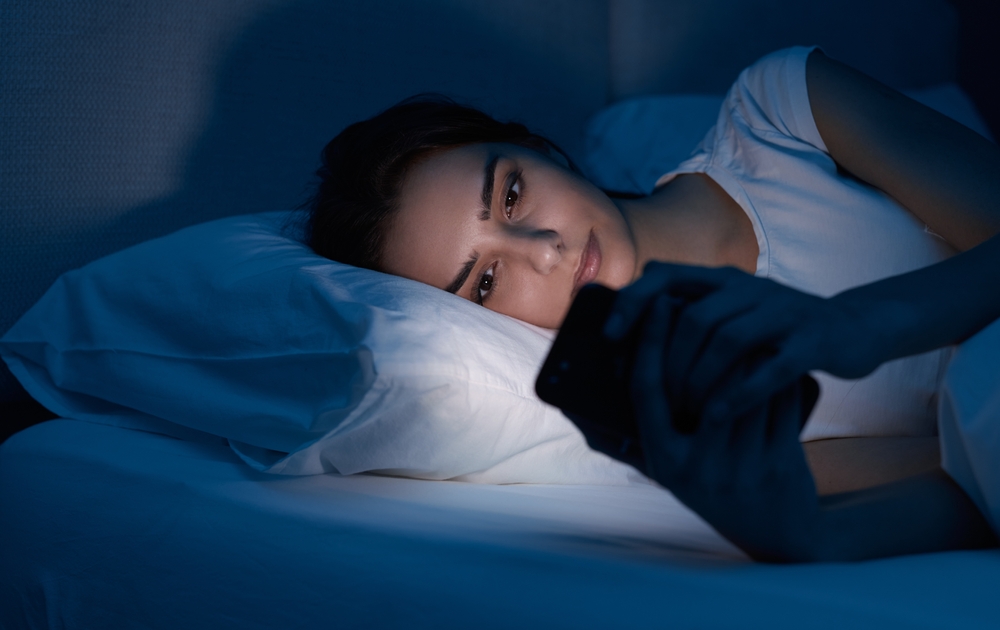 Woman looking at phone in bed with blue light shining on her skin